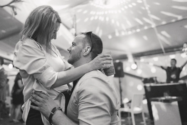Couple dancing tenderly under tent venue — black and white photography, intimate moment, reception lighting.