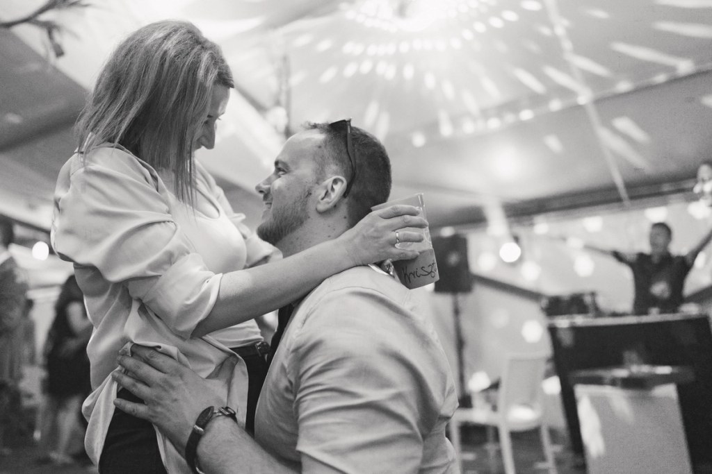 Couple dancing tenderly under tent venue — black and white photography, intimate moment, reception lighting.