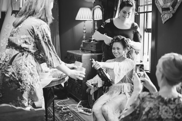 Bride laughing with a champagne bottle in hand, bridesmaids grinning around her