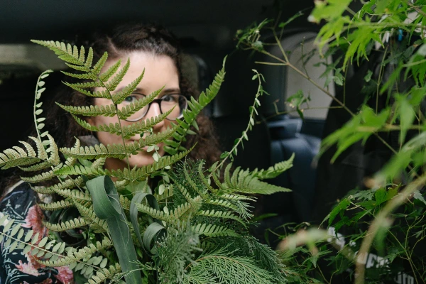 Close-up of a woman peeking through dense green fern leaves. Creative wedding detail photography.