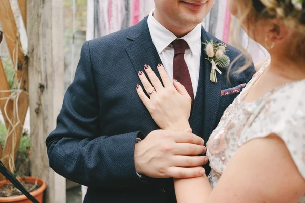 Groom in blue suit and bride in white lace close together, engagement ring visible