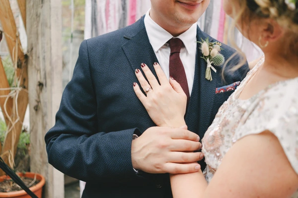 Groom in blue suit and bride in white lace close together, engagement ring visible