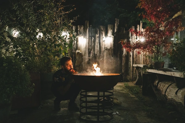 Man sits by the fire in the night garden, warm flames lighting his face