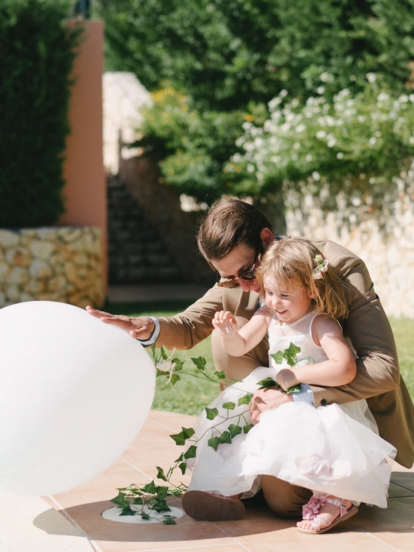 Young man and little girl play joyfully with a white balloon in the sunny garden