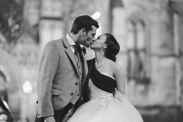 Bride and groom kiss on the wedding day — grey suit, white tulle skirt, blurred urban architecture
