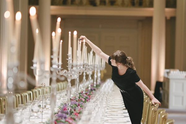 Woman in black lights candles at the elegantly set table — floral decoration, crystal glasses