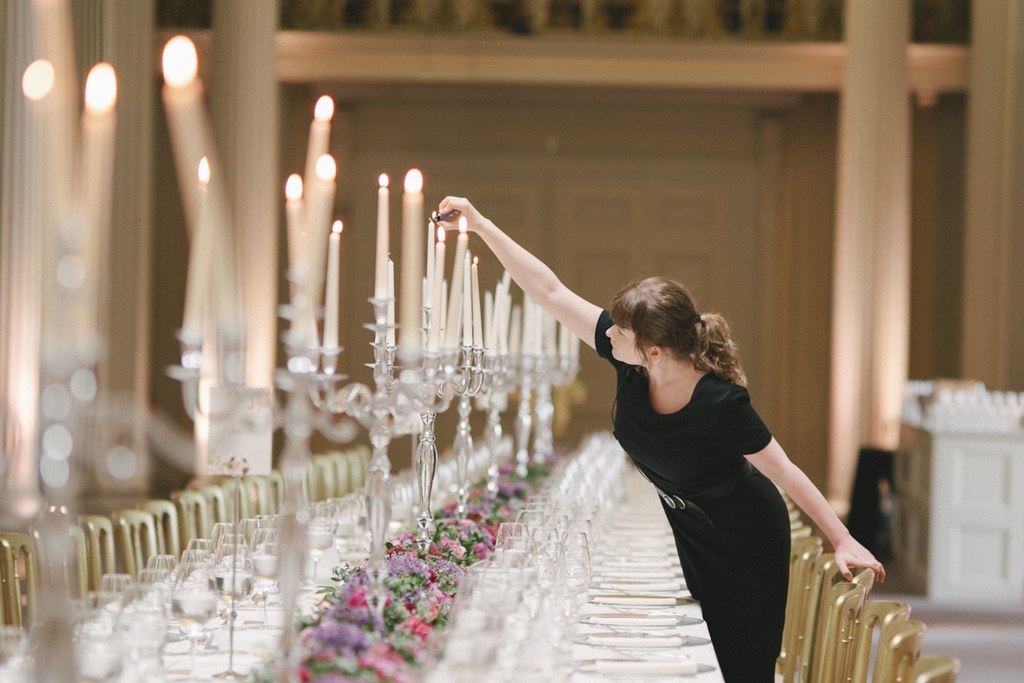 Woman in black lights candles at the elegantly set table — floral decoration, crystal glasses