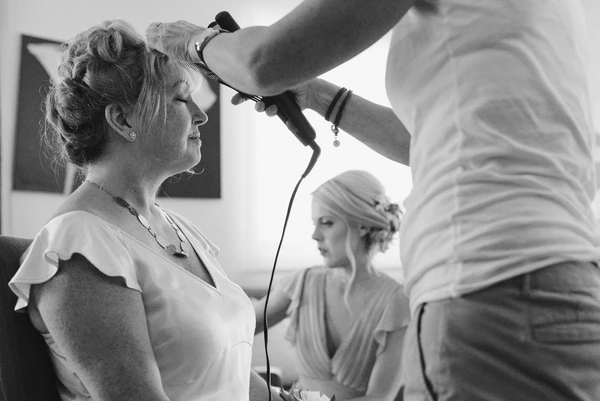 Bride being made up before the ceremony, makeup artist beside her — black-and-white