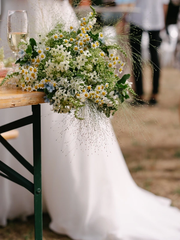 Close-up of white daisy and foliage wedding floral arrangement on wooden chair at outdoor ceremony.