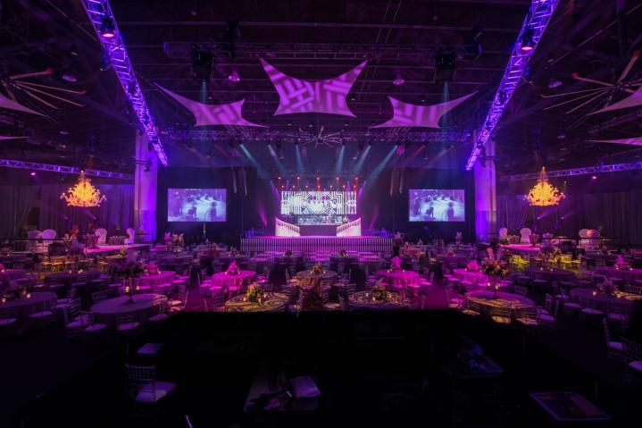 Corporate event with dramatic lighting, elaborate stage design featuring large screens, and artistic decor throughout.