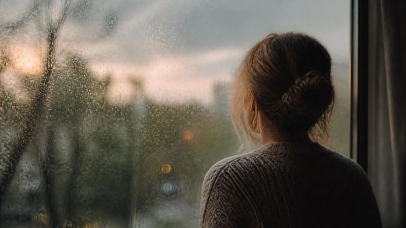 A woman looking thoughtfully out a rain-streaked window, representing the emotional impact of menopause