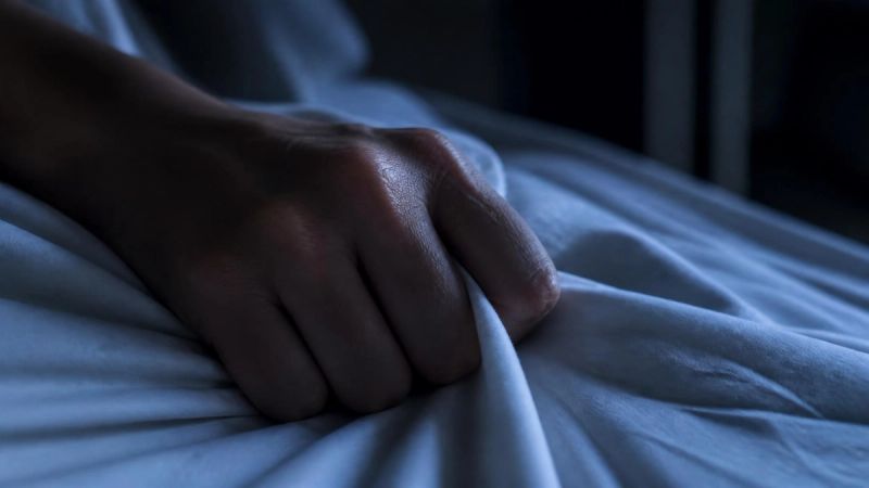 A close-up of a person's hand gripping bedsheets at night, tension and anxiety