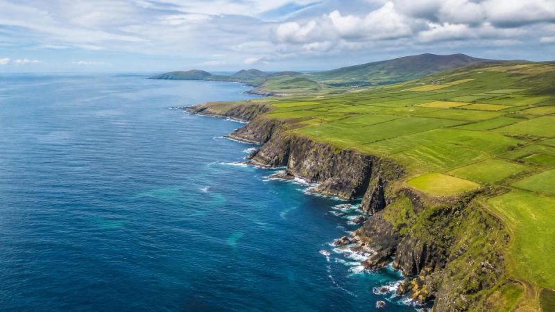 A view of the Irish coastline from above with green fields and blue sea, representing island life and the need to fly