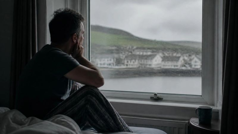 A person sitting alone by a window on an overcast Irish day, conveying low mood and insomnia