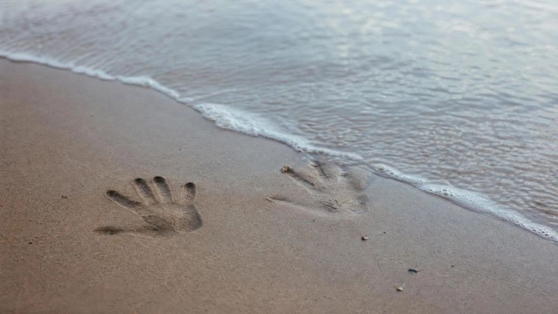 Two overlapping hands drawn in sand at an Irish beach, one fading, symbolising grief and loneliness