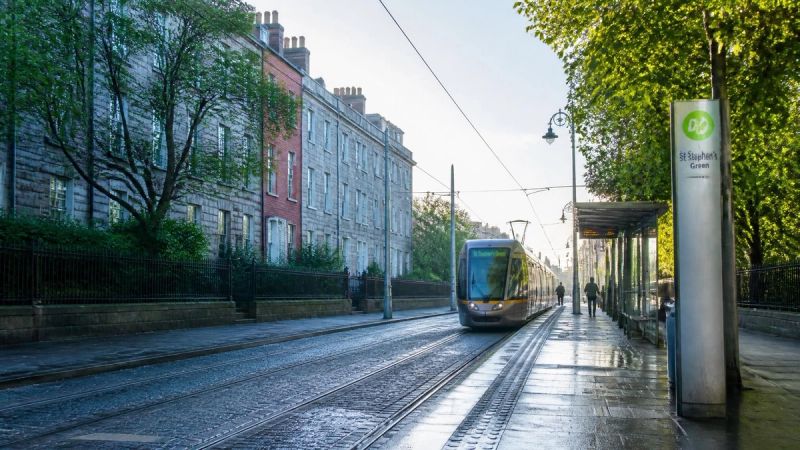 A quiet Irish street or LUAS platform with soft light, representing travel and public life challenges