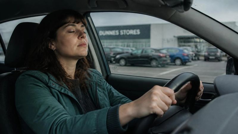 A person sitting in a car with hands on the steering wheel, taking a slow breath