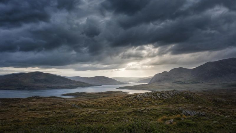 Storm clouds gathering over a quiet Irish landscape, symbolising prolonged adversity and the causes of C-PTSD