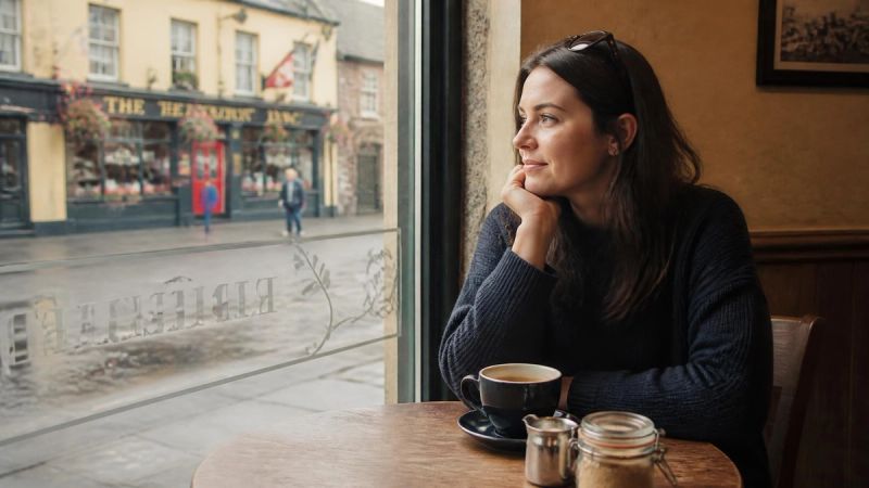 A person sitting alone at a café table by a window with a coffee, relaxed and thoughtful