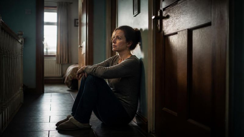 A parent sitting beside a closed bedroom door, looking worried but patient