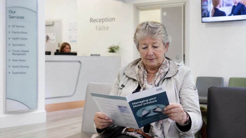 A senior adult sitting in a GP waiting room looking at health information