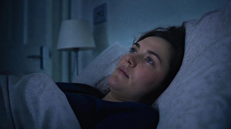 A person lying awake in bed at night, eyes open, looking at the ceiling
