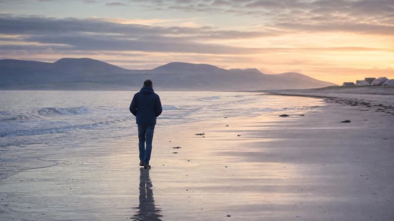 A single person walking on a quiet Irish beach at dawn, representing the hidden mental load carried by partners