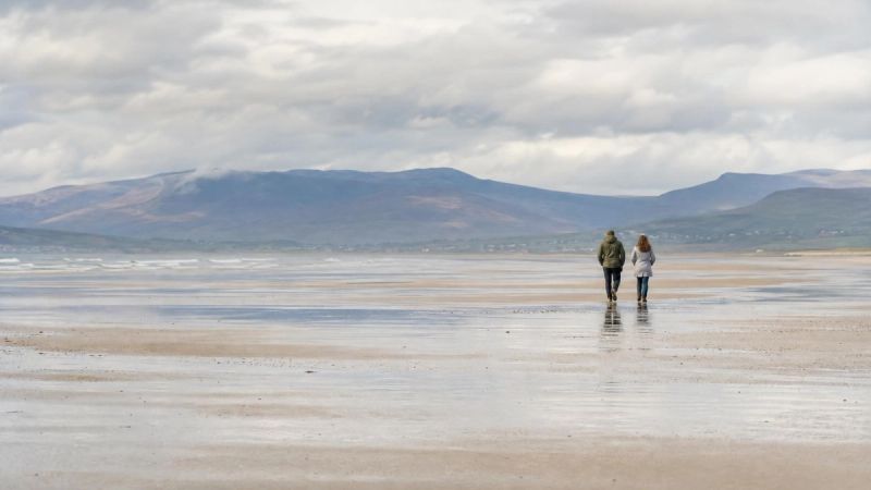 Two people walking together along a wide Irish beach at low tide, representing quality connection without forcing it