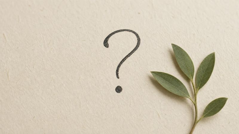 A handwritten question mark on cream paper with a small green leaf