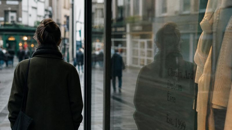 Person's reflection in a shop window in an Irish city, representing self-evaluation and appearance-based comparison