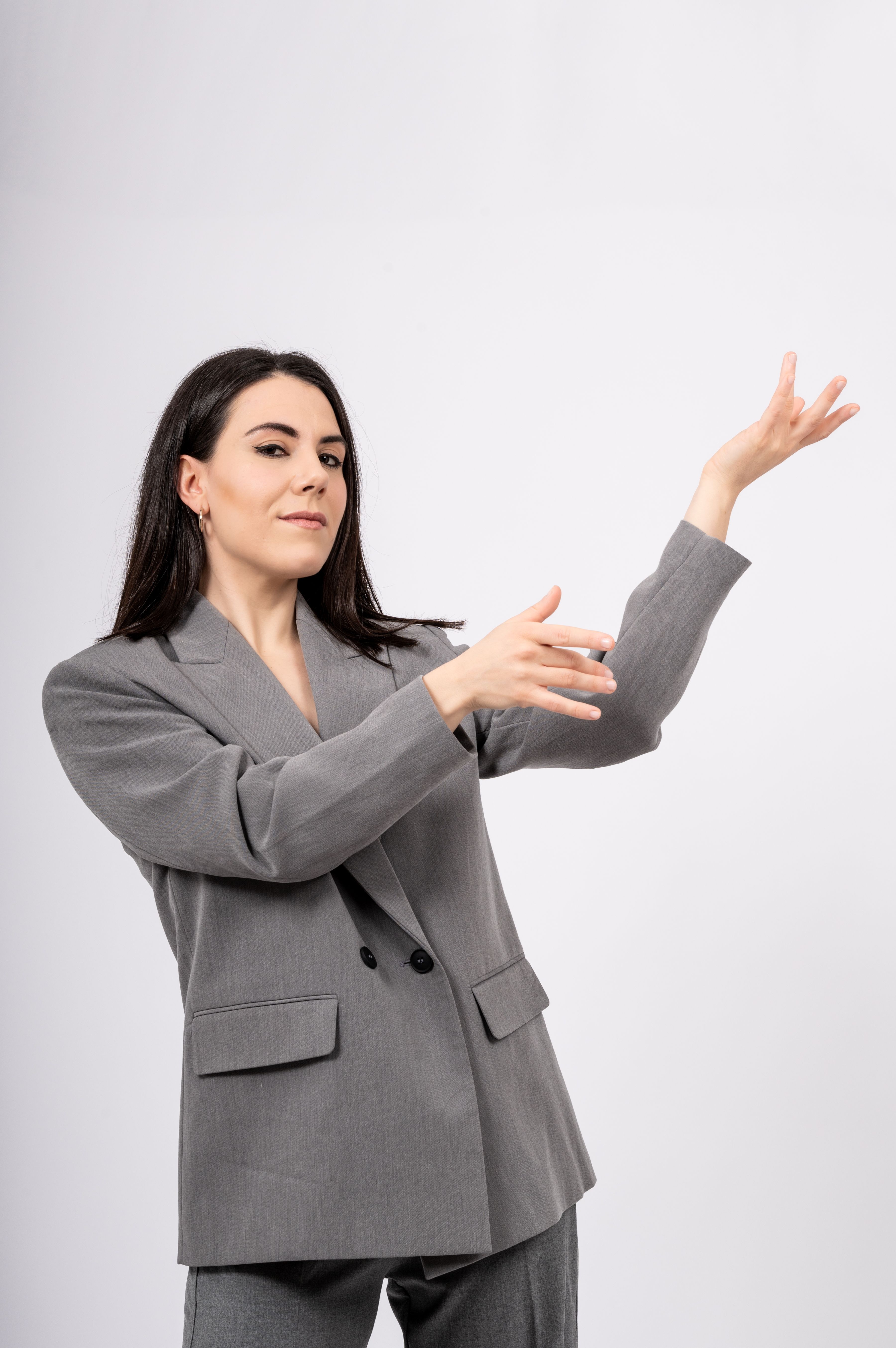 Sonja Reisch l(Tänzerin und Choreographin des Stückes Liberatio), eine Frau mit langem braunen Haaren, kreiert in einem grauen Anzug eine elegante Pose mit ihren Händen