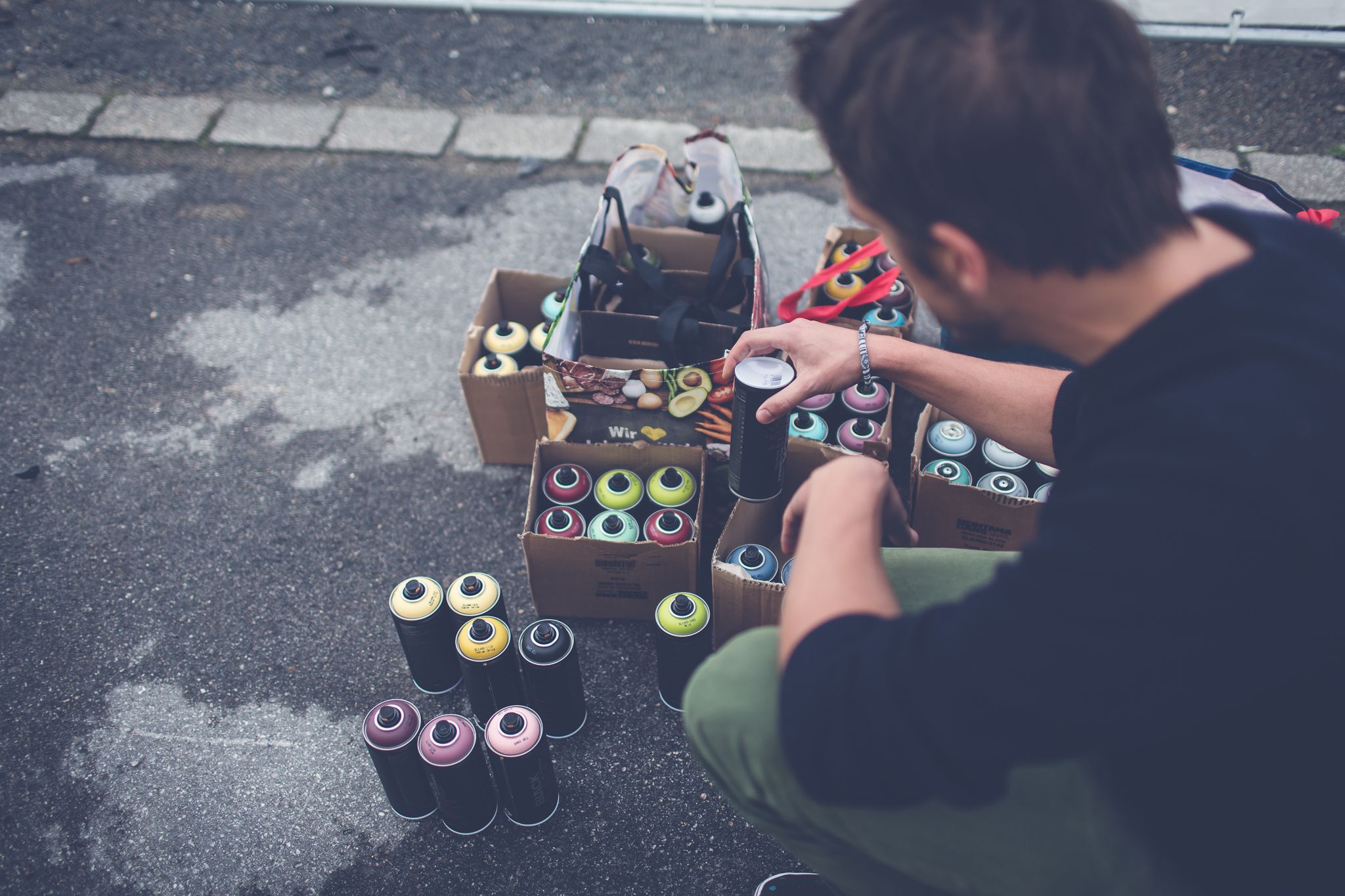 Person aus der Rückansicht mit einer Spraydose in der Hand und weiteren vor sich