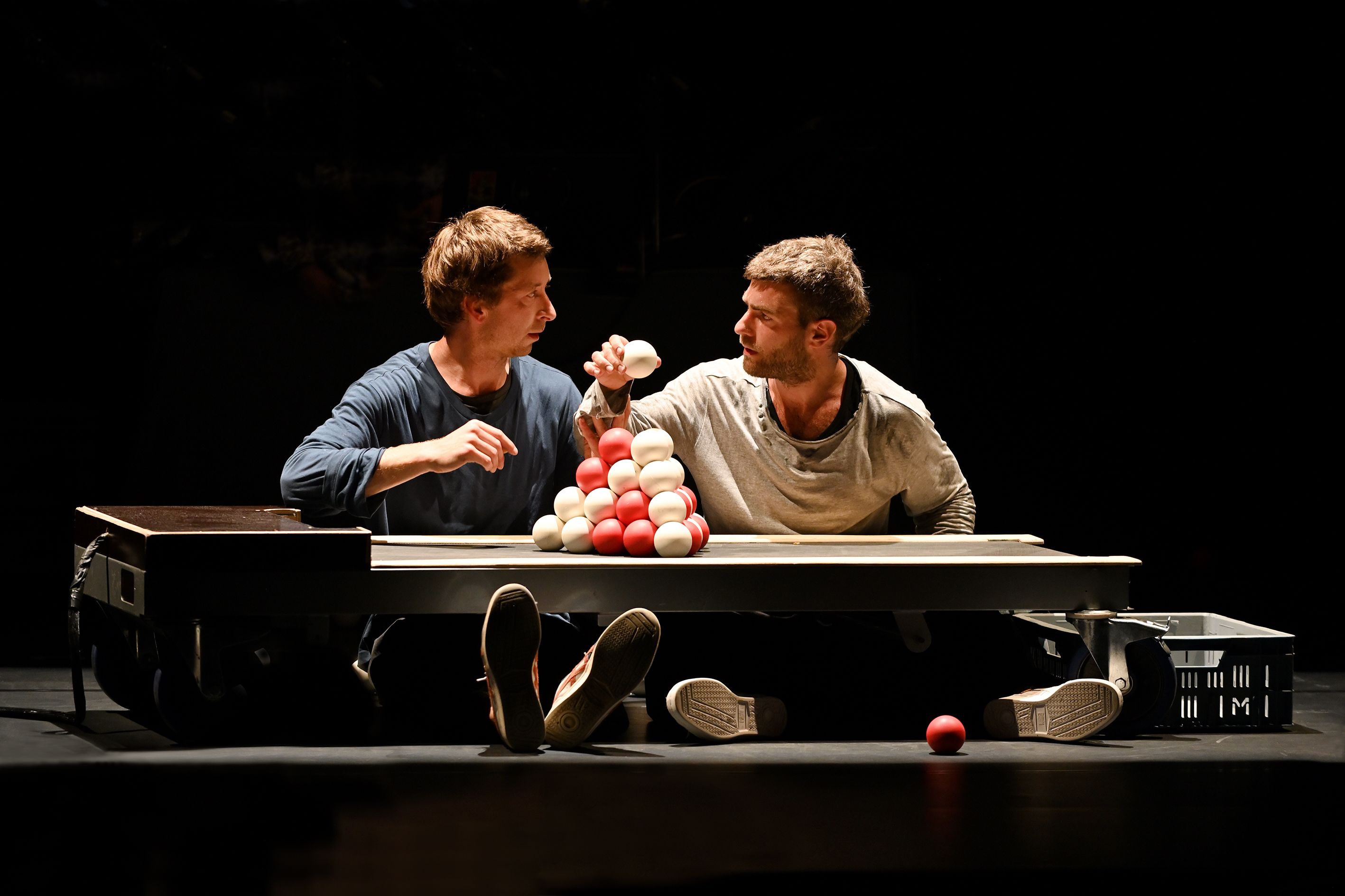 Zu sehen sind zwei Personen mit einem Haufen von Jonglierbällen vor ihnen. Die zwei Personen schauen sich ins Gesicht.