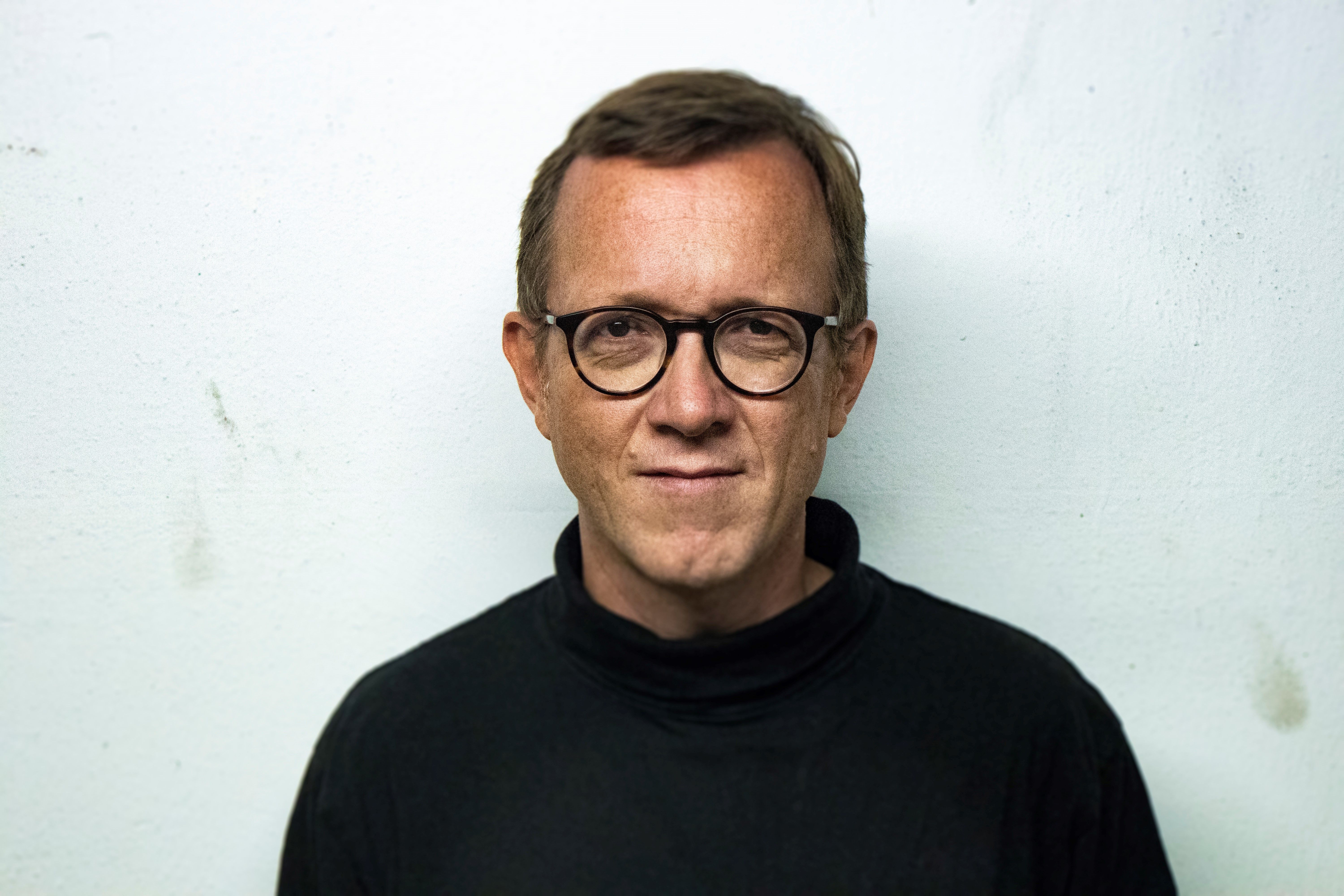 Das Foto zeigt eine Nahaufnahme in Form eines Portraits von einem leicht lächelnden Heiner Kruse. Heiner Kruse trägt darauf einen schwarzen Rollkragenpullover und eine dunkle rundliche Brille.