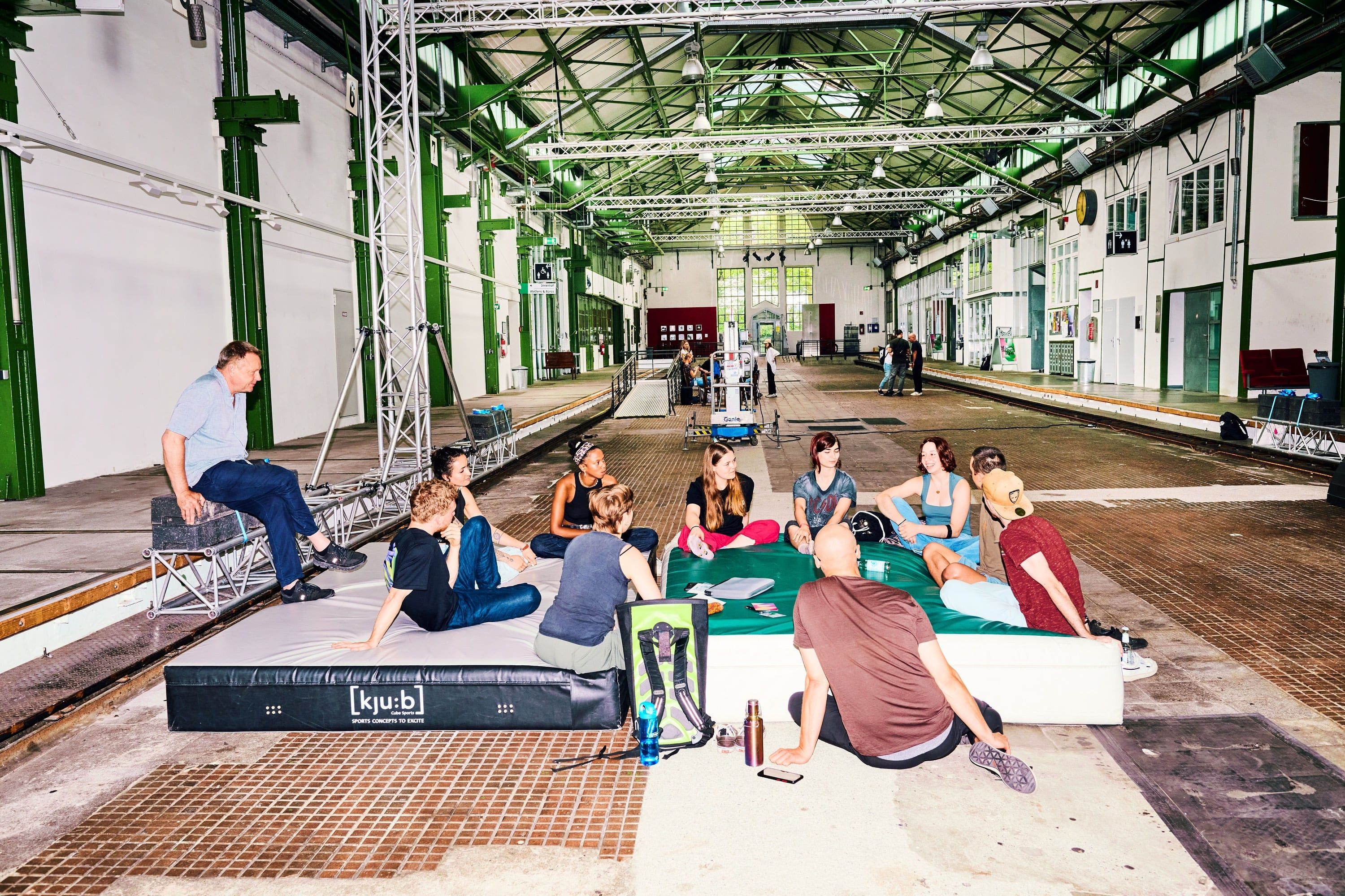 Jugendliche, die in einer Industriehalle auf zwei Matten auf dem Boden im Kreis sitzen