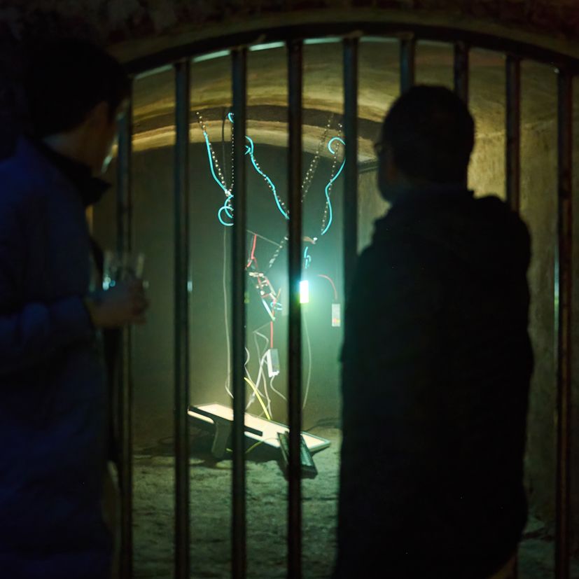 zwei Personen, die in einen Raum in einem Keller schauen, in dem eine Lichtinstallation hängt