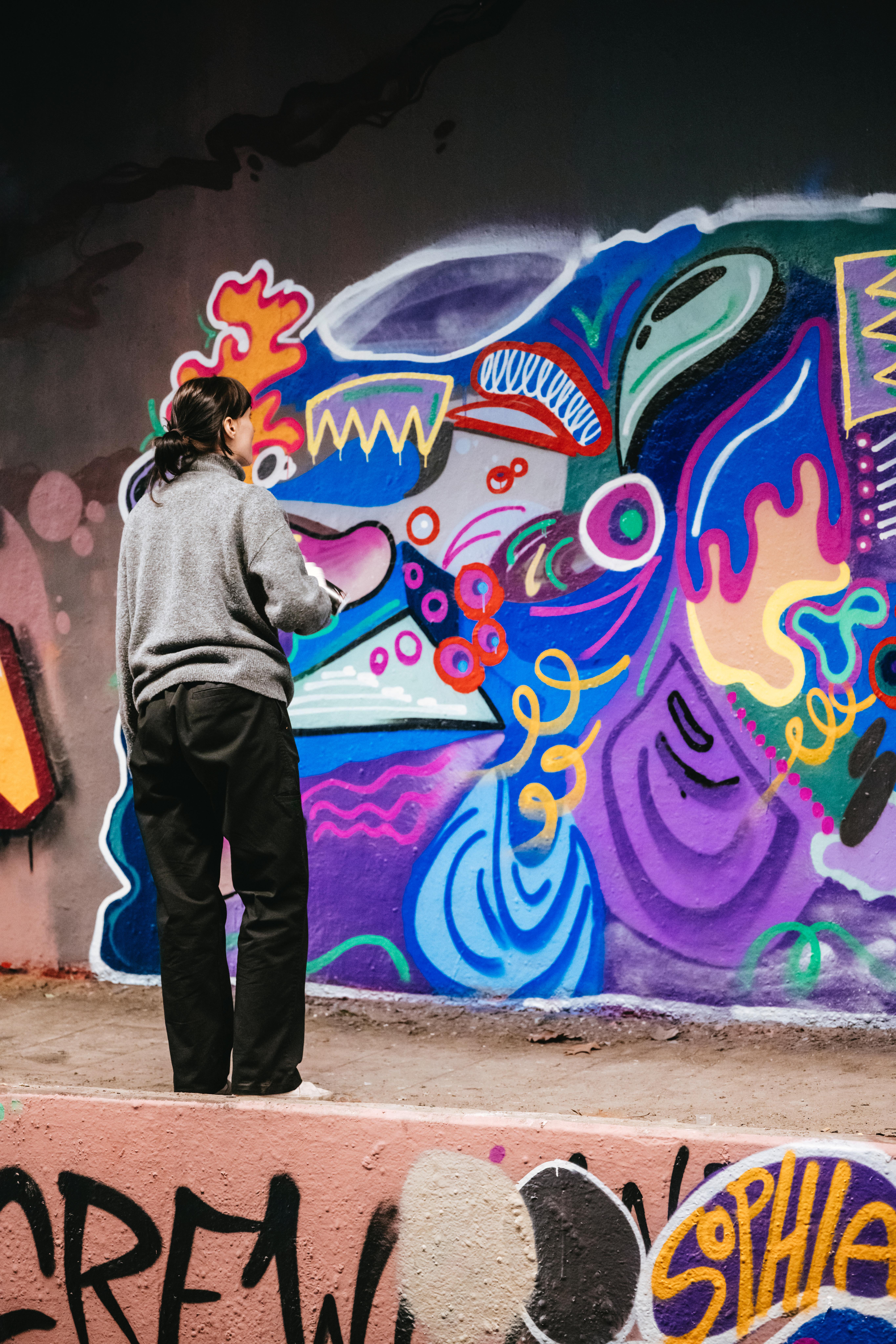 Zu sehen ist eine Person vor einer Wand. Sie malt ein Graffiti.