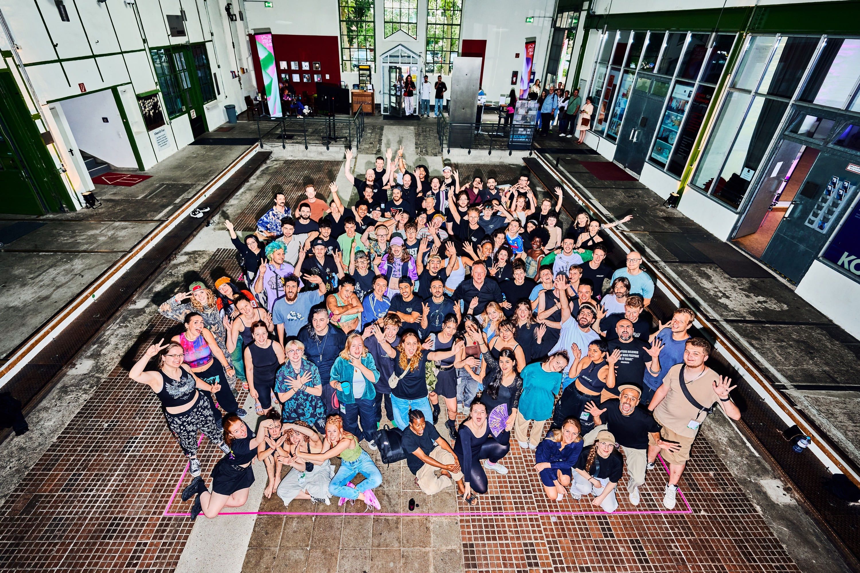 Group photo of participants standing in the middle of a hall and waving at the camera