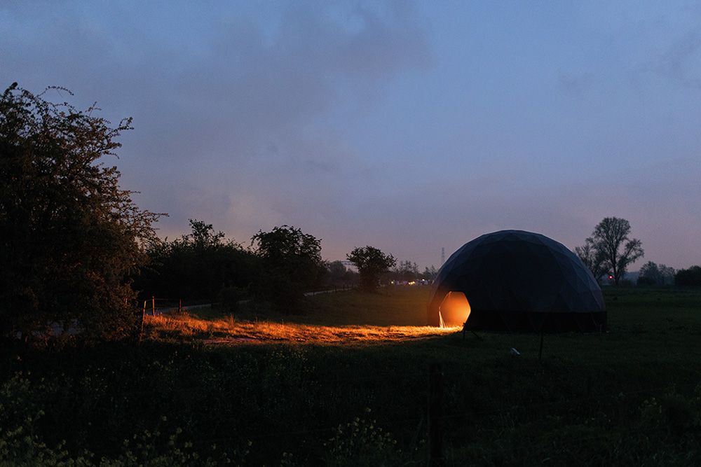 A dome can be seen. There is an entrance to the dome on the side. Warm light streams out of the dome and casts a beam of light into the darkness.