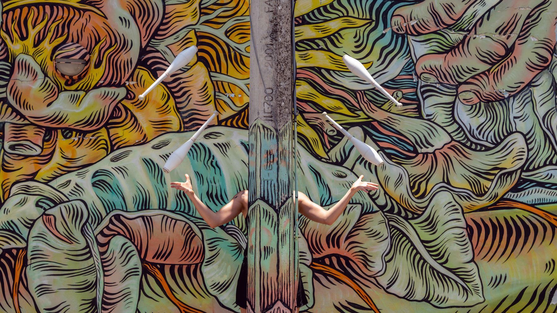 Juggler hidden by a pillar juggling in front of wall with animal motifs