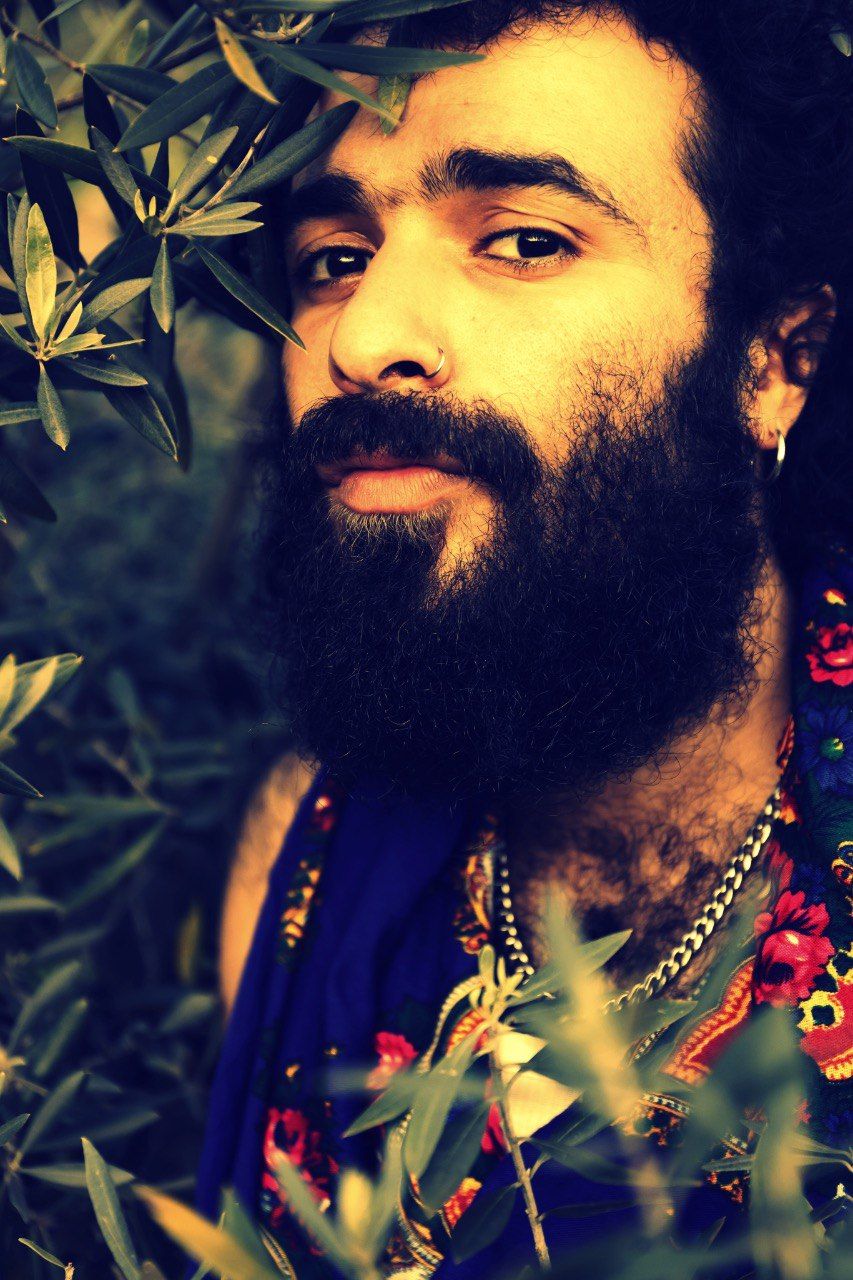 The picture is a portrait of a person with dark hair surrounded by olive branches and wearing a Kurdish scarf.