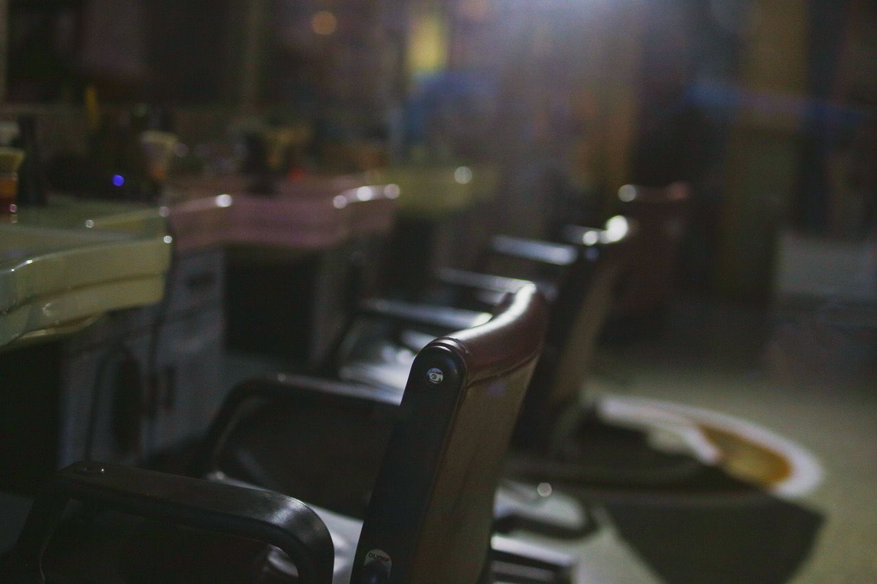 Leather chairs placed in front of a mirror and a shelf with utensils in a hair salon