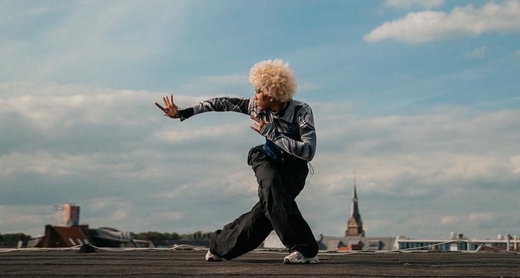 A person is probably standing on a roof. Other rooftops can be seen in the background. The person in the picture is dancing.