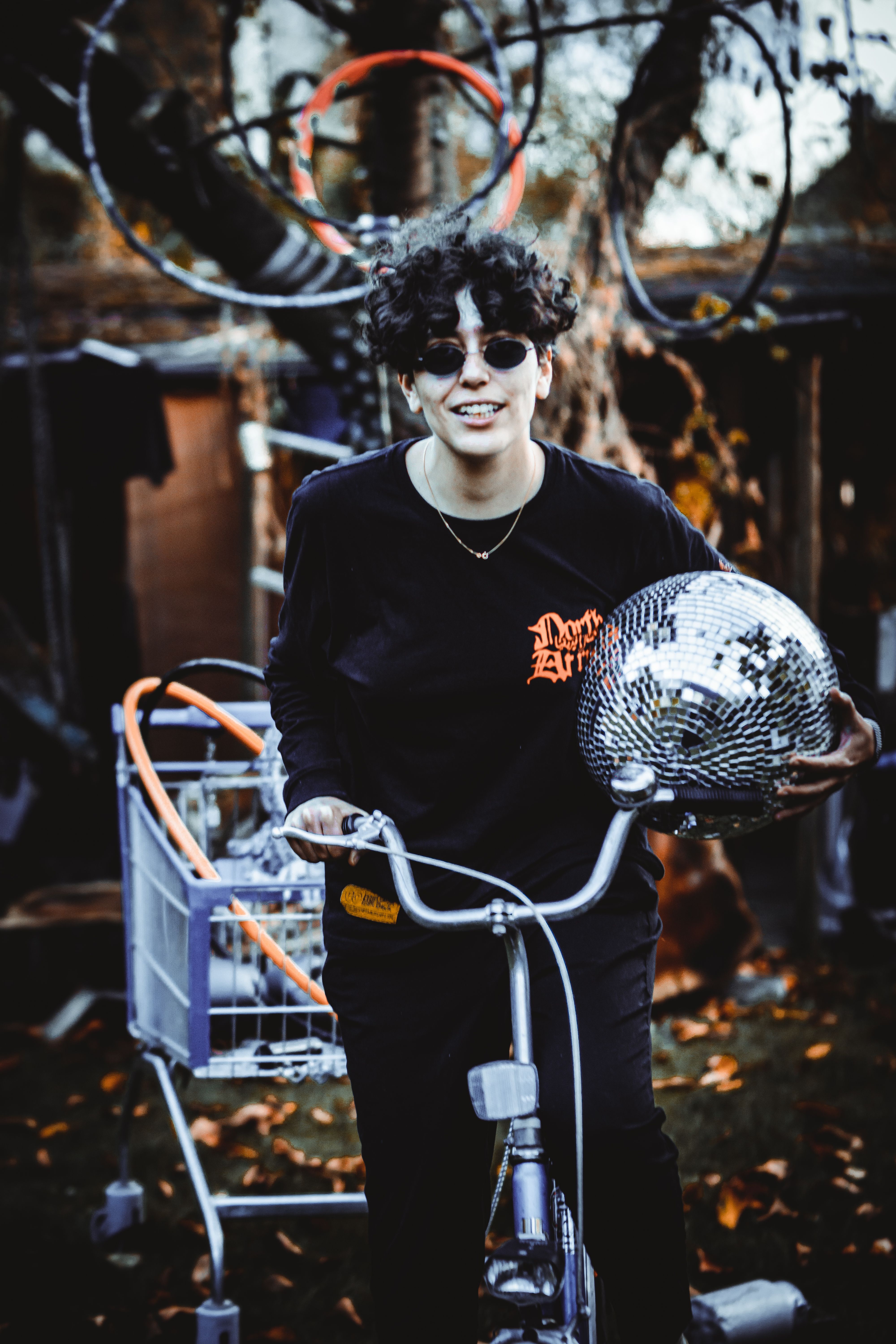 The picture shows a person in black clothing sitting on a bicycle and holding a disco ball in their left hand.