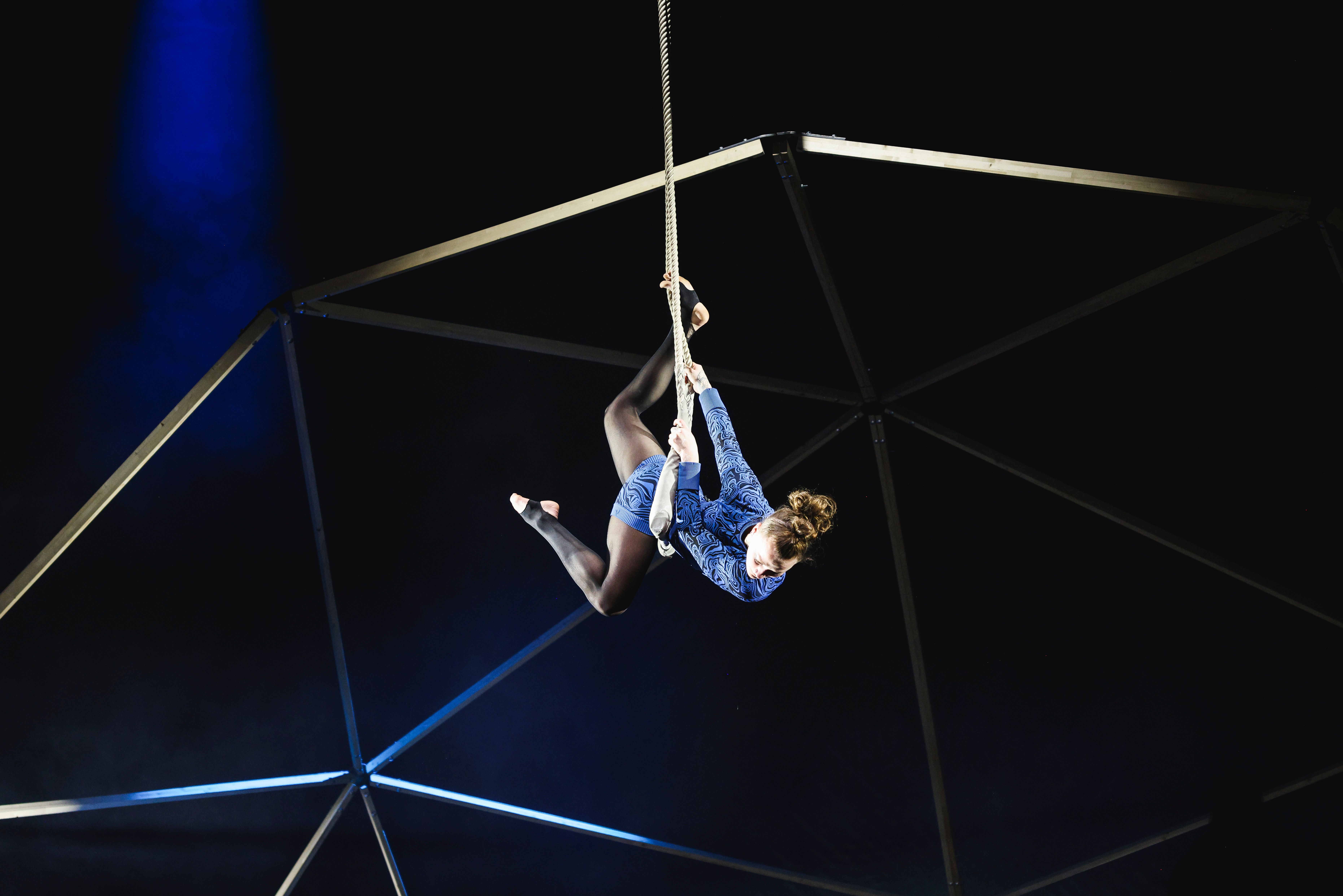 An acrobat hangs on a rope during a performance.