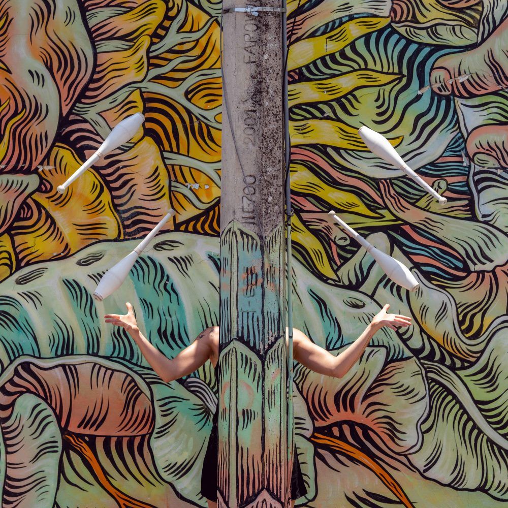 Woman hidden and juggling in front of a designed background