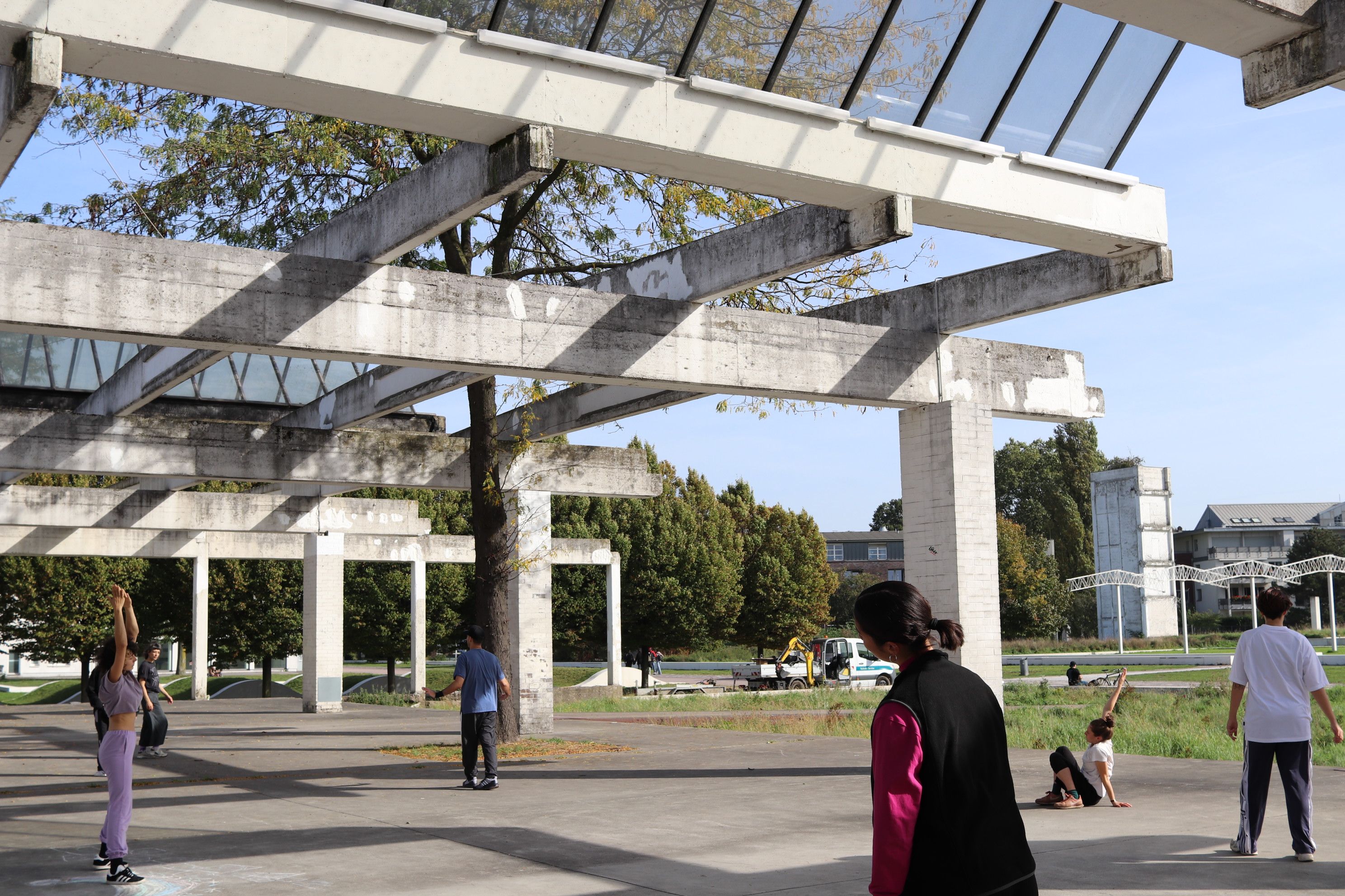 Young people are dancing outside on paved ground in a play of sunlight and shadow