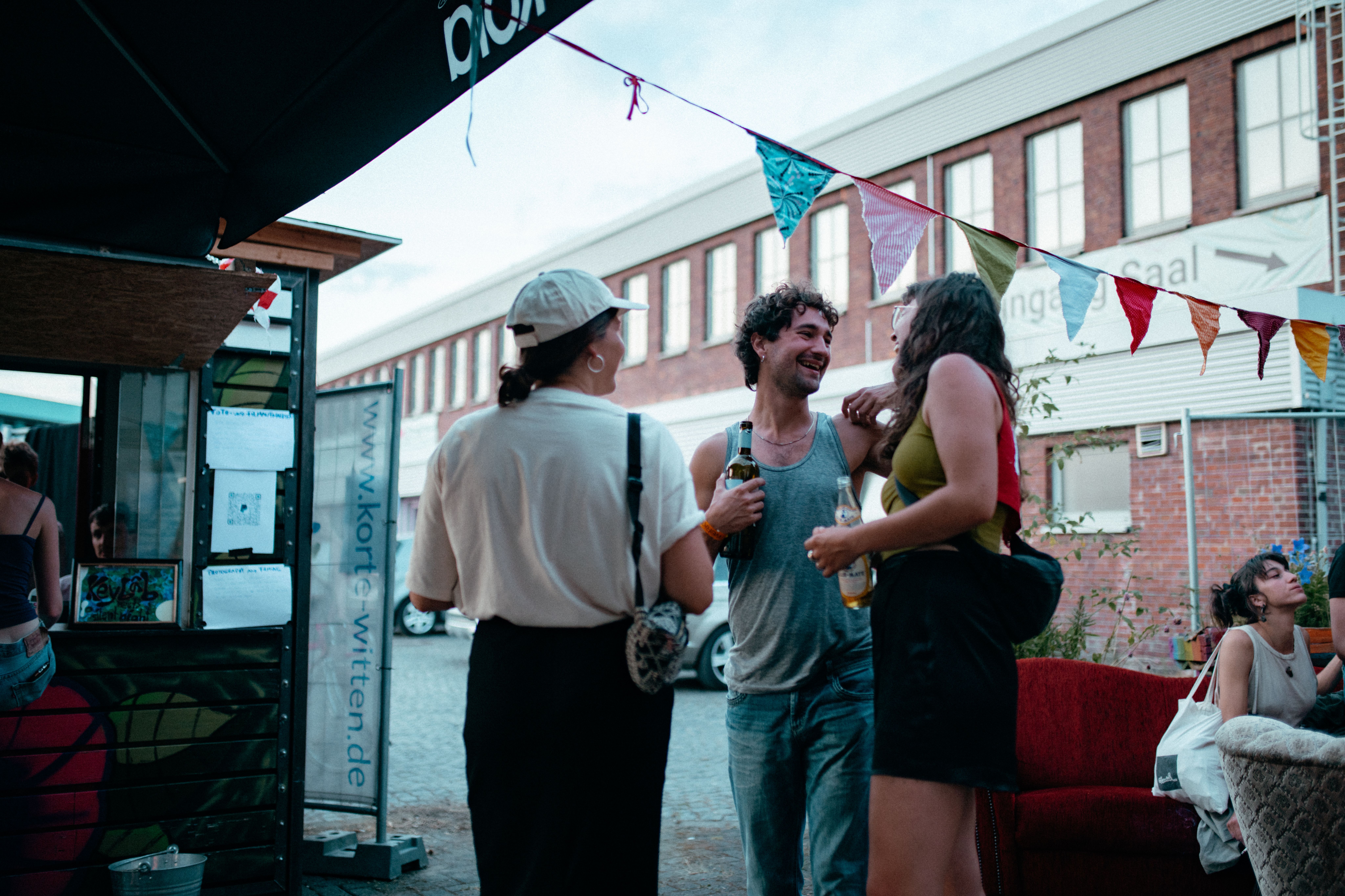 The picture shows three people at an event. They are facing each other, holding drinks in their hands while laughing.