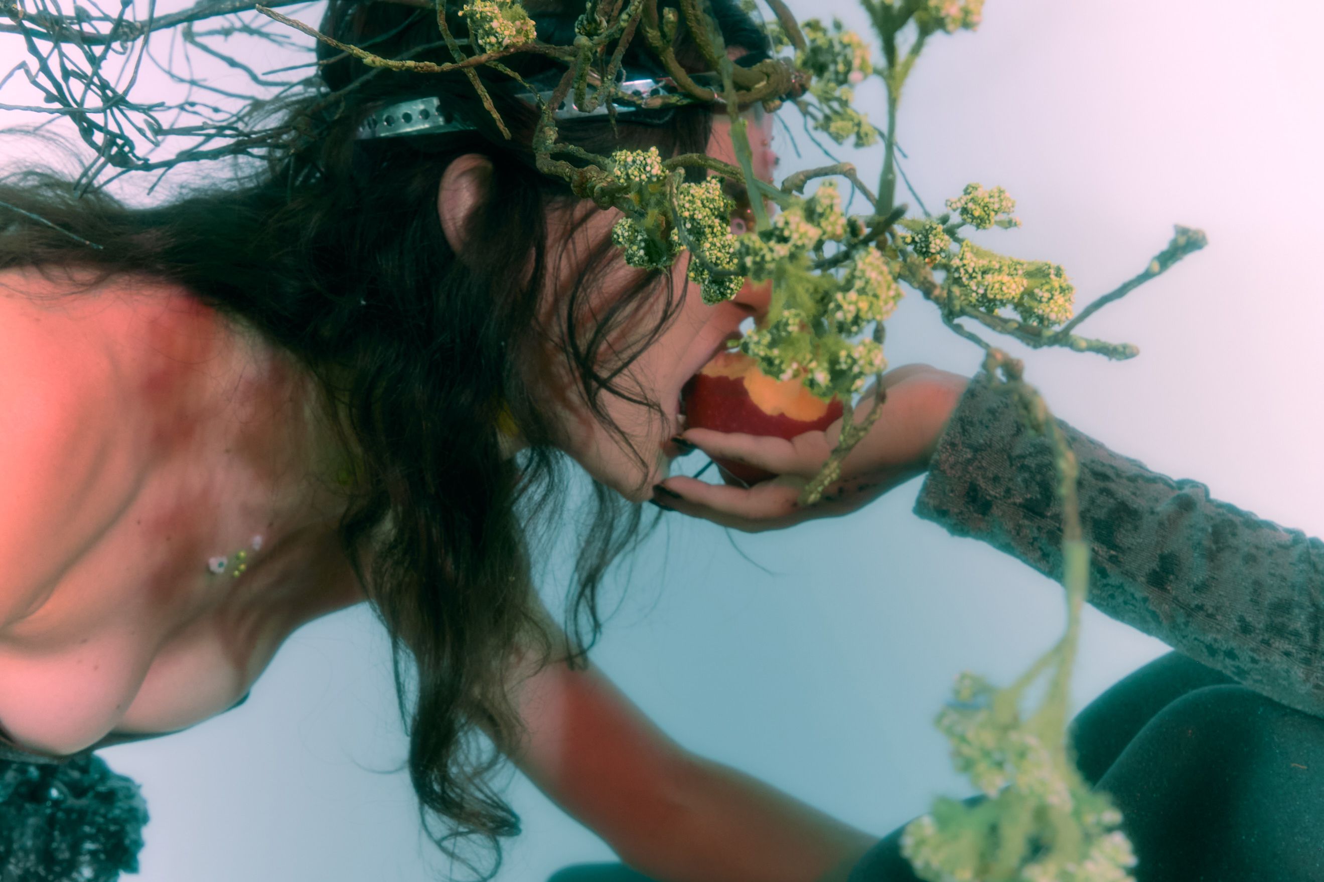 You can see a person with twigs in her hair. They are biting into an apple that is being handed to them.