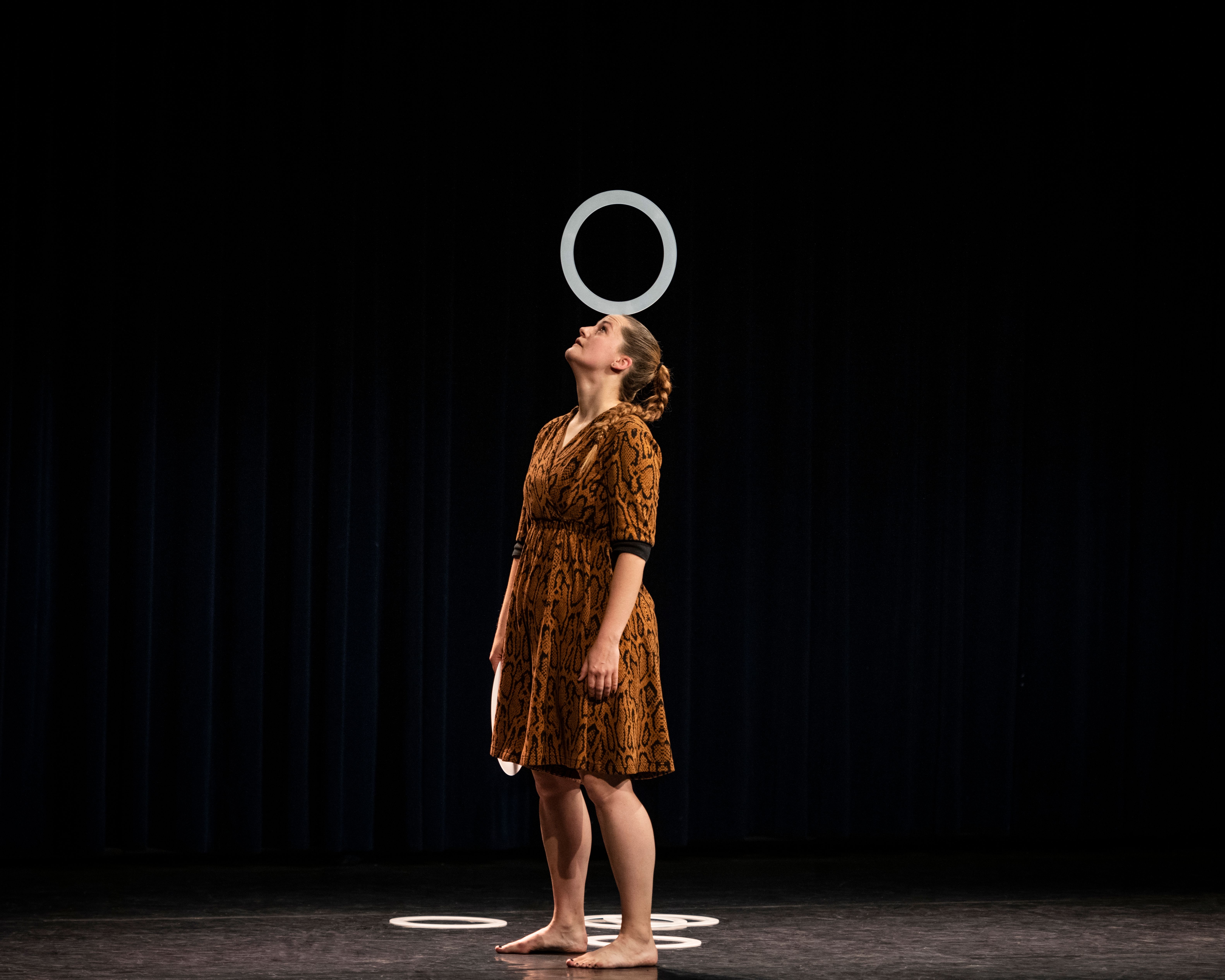 You can see an artist with a ring that she is balancing on her face. She looks up at the ceiling.